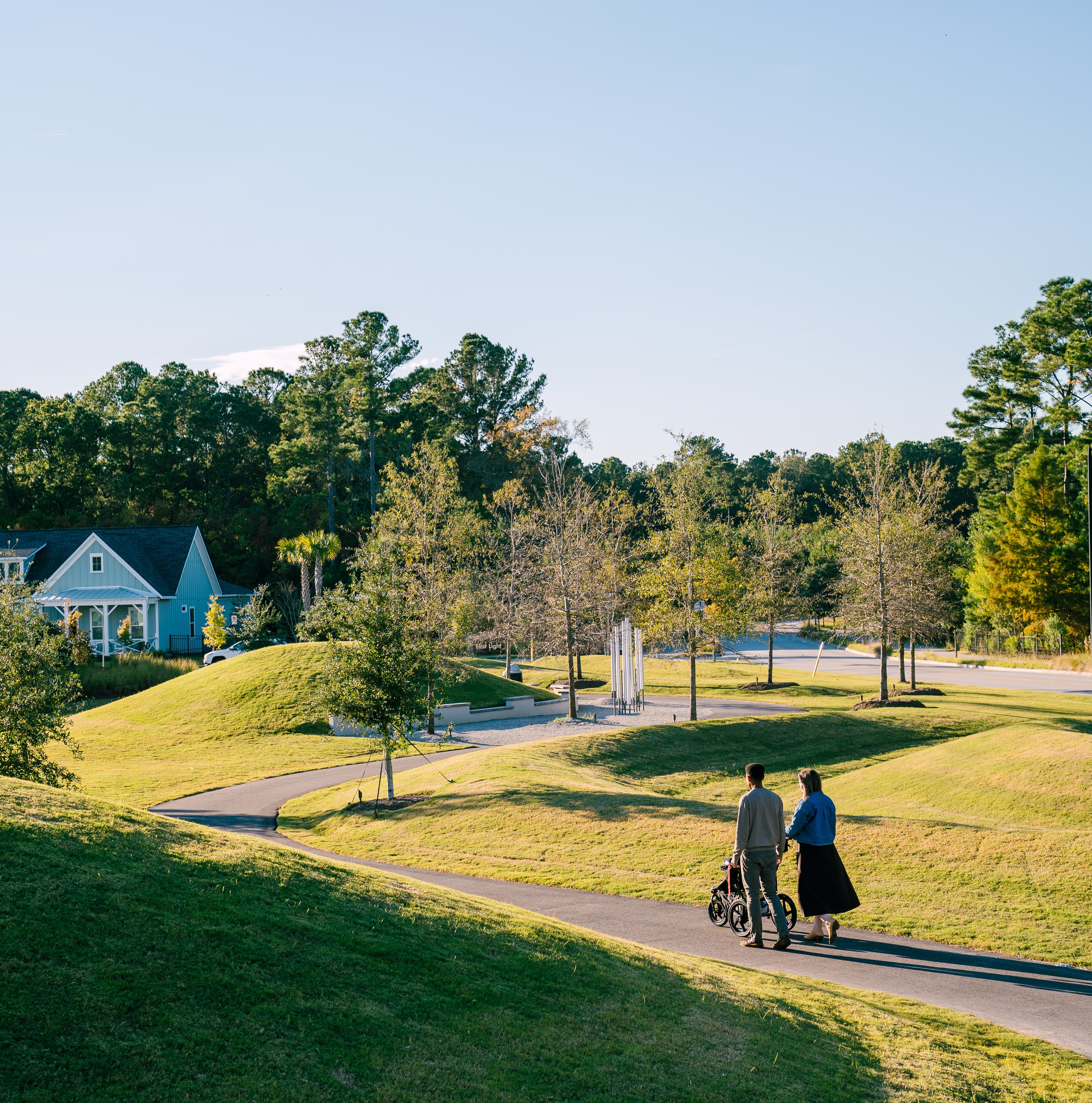 Residents enjoy a walk along a landscaped trail in Point Hope, a master-planned community in Charleston, South Carolina, featuring green spaces, rolling lawns, and new construction homes.